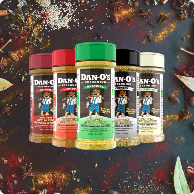 Five jars of Dan-O’s seasoning blends against a background of loose spices. 