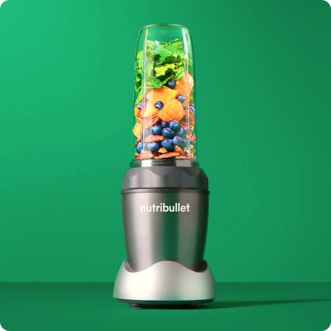 A Nutribullet blender filled with fruits and vegetables on a green background.